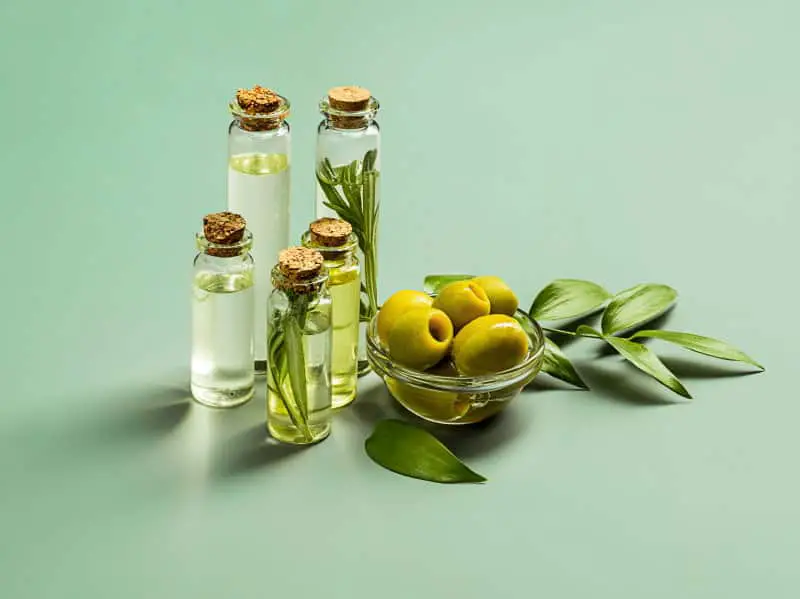 Olive oil and olive branch on the green wooden table and green background